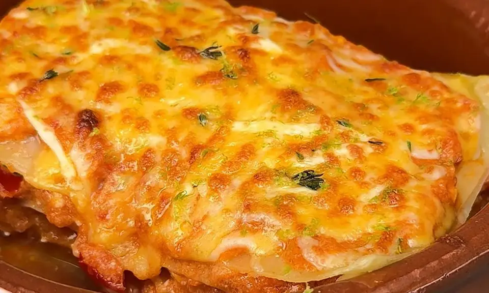 Deliciosa lasaña de atún gratinada con queso dorado y hierbas frescas, servida en un cuenco de barro.