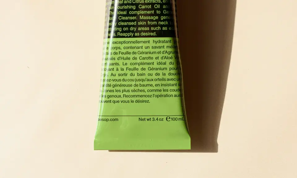 Tubo verde brillante di Aesop con testo in inglese e francese. Il testo descrive un balsamo corpo idratante, spiegando il suo inci significato e gli ingredienti chiave.