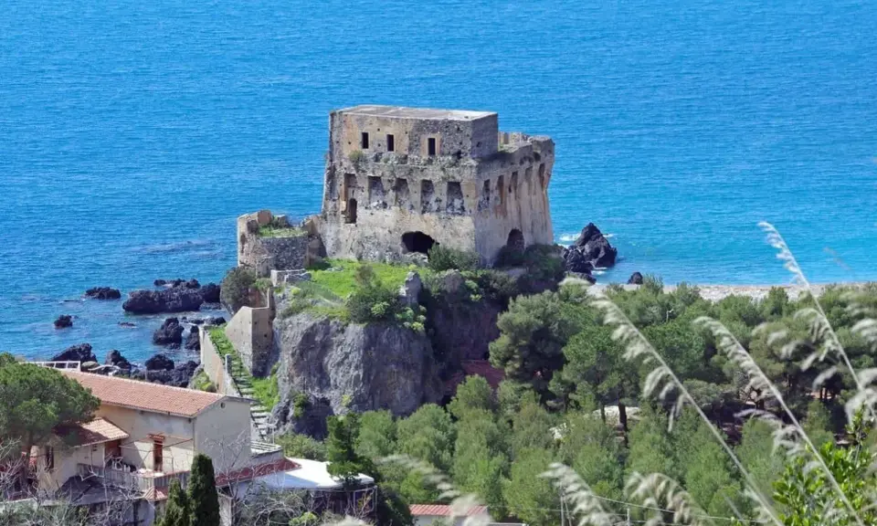 Torre aragonese a picco sul mare, uno dei borghi da visitare in Calabria, con case e vegetazione lussureggiante.