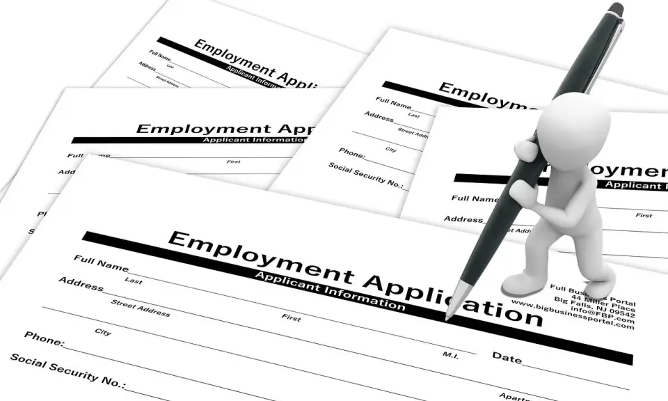 Biała figurka z długopisem wypełnia formularz "Employment Application" (ogłoszenie o pracę po ang.).