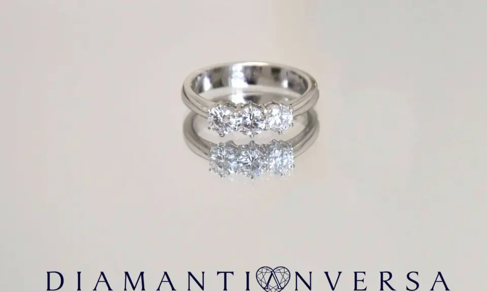 Un anello prezioso con tre diamanti scintillanti, riflesso su una superficie lucida.