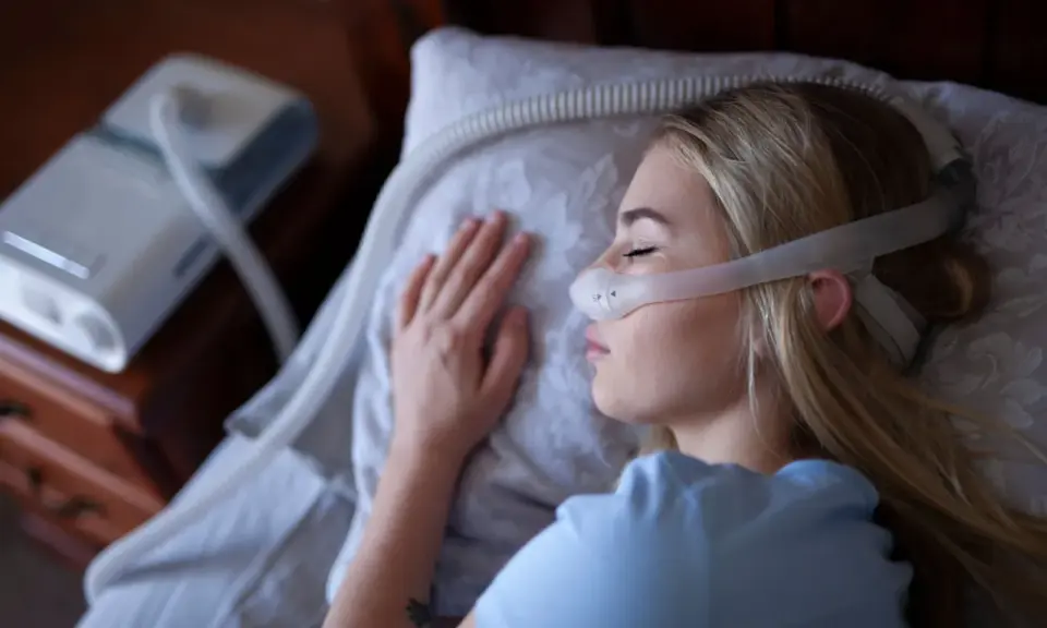Kobieta śpi z maską CPAP, która jest protezą na NFZ, zapewniając jej spokojny sen.