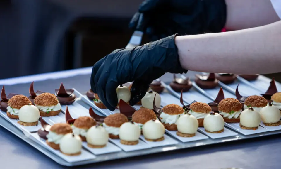 Mains de chef en gants noirs disposant des bouchées, une spécialité culinaire de Metz, sur un plateau.