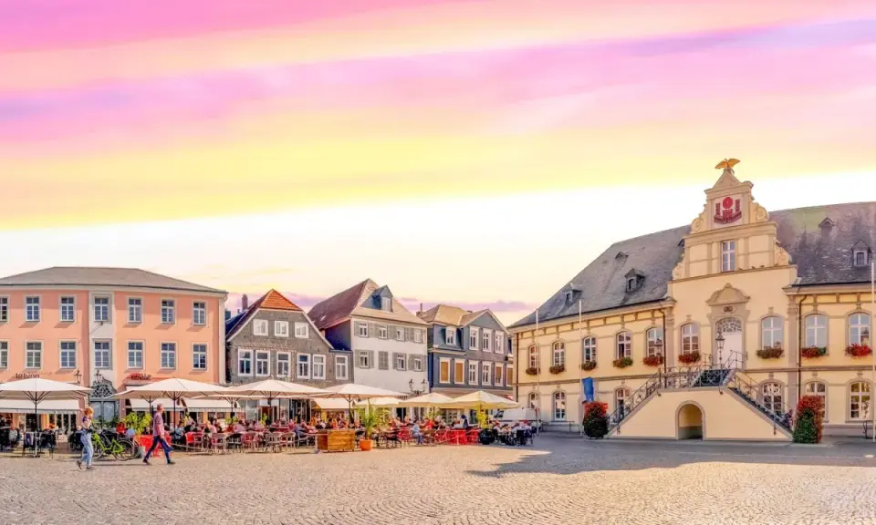 Ein Marktplatz mit Cafés und historischen Gebäuden, der an das "Venedig Westfalens" erinnert, unter einem farbenfrohen Himmel.