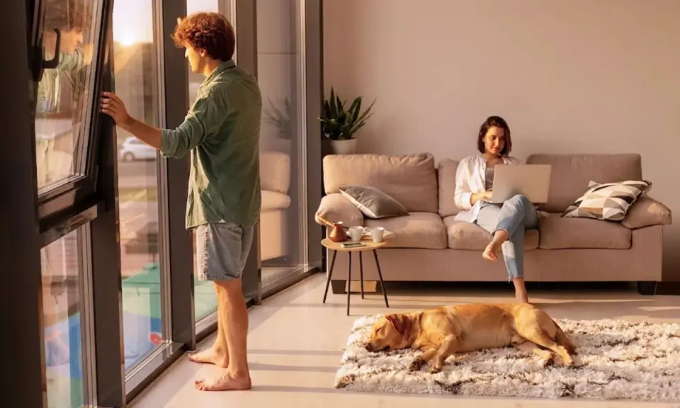 Hombre abre ventana, mujer trabaja en laptop en sofá, perro duerme. El ruido exterior, 40 dB es mucho ruido, interrumpe la paz.