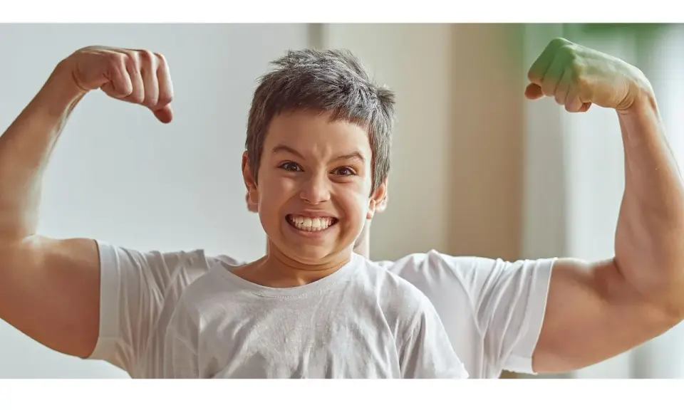 Chłopiec z miną jak po **buncie 5 latka** pokazuje swoje małe bicepsy, podczas gdy za nim widać potężne ramiona taty.