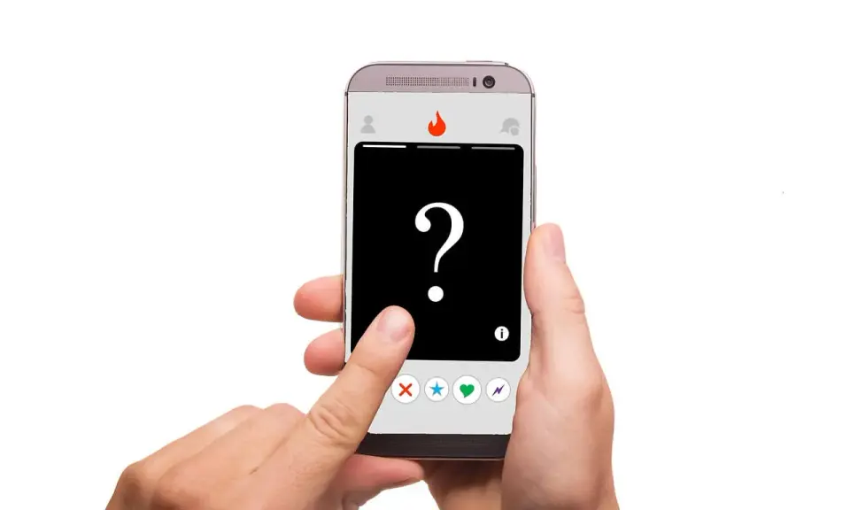 Dłoń trzyma smartfon z aplikacją randkową. Na ekranie znak zapytania i ikony: X, gwiazdka, serce, błyskawica – typowe oznaczenia na Tinderze.