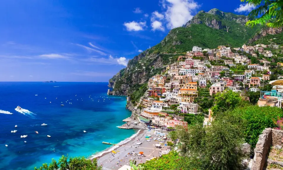 Positano, un gioiello incastonato tra il verde dei monti e l'azzurro del mare in Campania. Case colorate a picco sul mare, una spiaggia affollata e barche che solcano le acque cristalline.