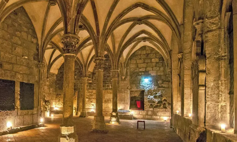 Gewölbte Gänge in einem **kloster mittelalter**. Säulen tragen das steinerne Dach, Kerzenlicht erhellt den Boden.