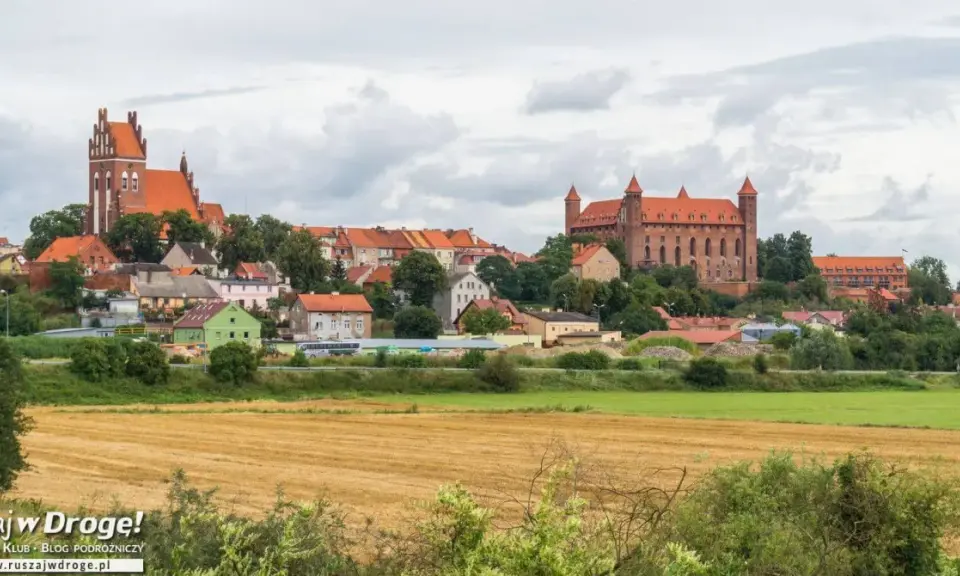 Widok na miasteczko z ceglanymi zamkami i kościołami, otoczone zielenią. W oddali pola uprawne. Wspaniałe **atrakcje** czekają na odkrycie!