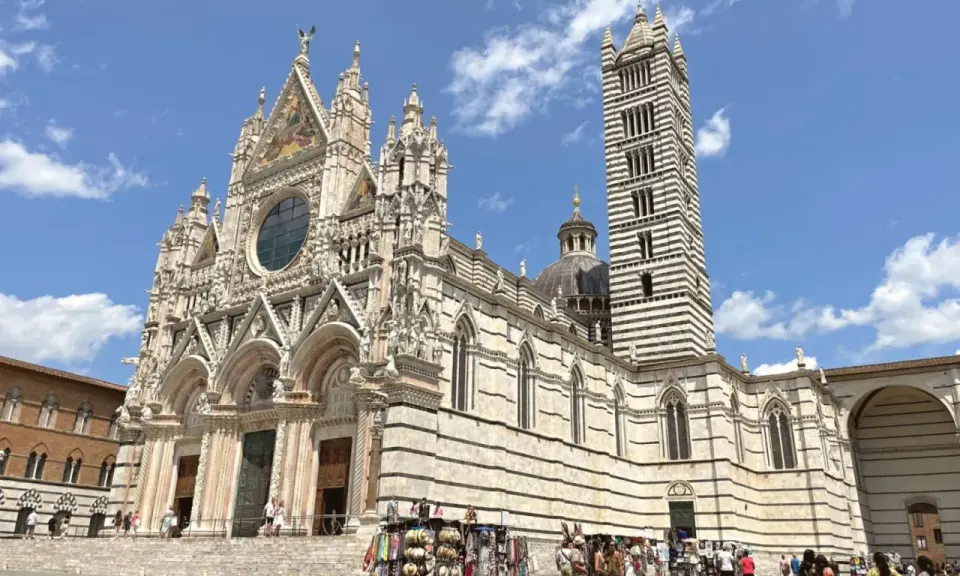 Il Duomo di Siena, con la sua imponente torre campanaria a strisce, è un must per chi cerca cosa visitare a Siena. La piazza antistante è animata da bancarelle.