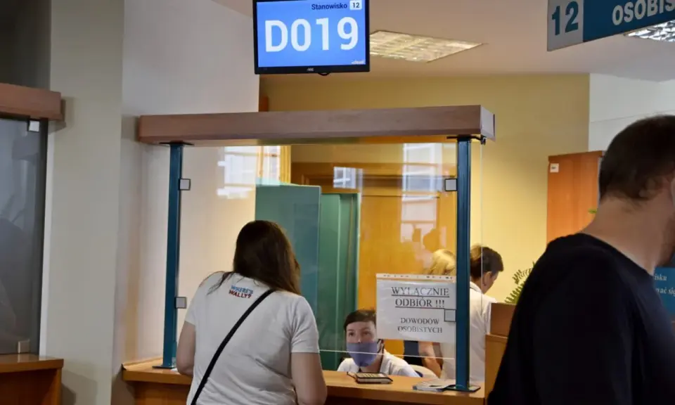 Kobieta czeka na odbiór dowodu rejestracyjnego. Na ekranie wyświetla się numer stanowiska D019.