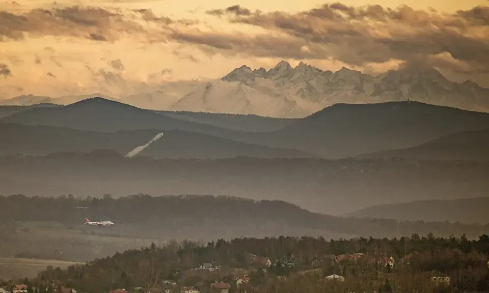 Widok na Tatry z Krakowa. Samolot leci nad mglistymi wzgórzami, a za nimi widać ośnieżone szczyty.