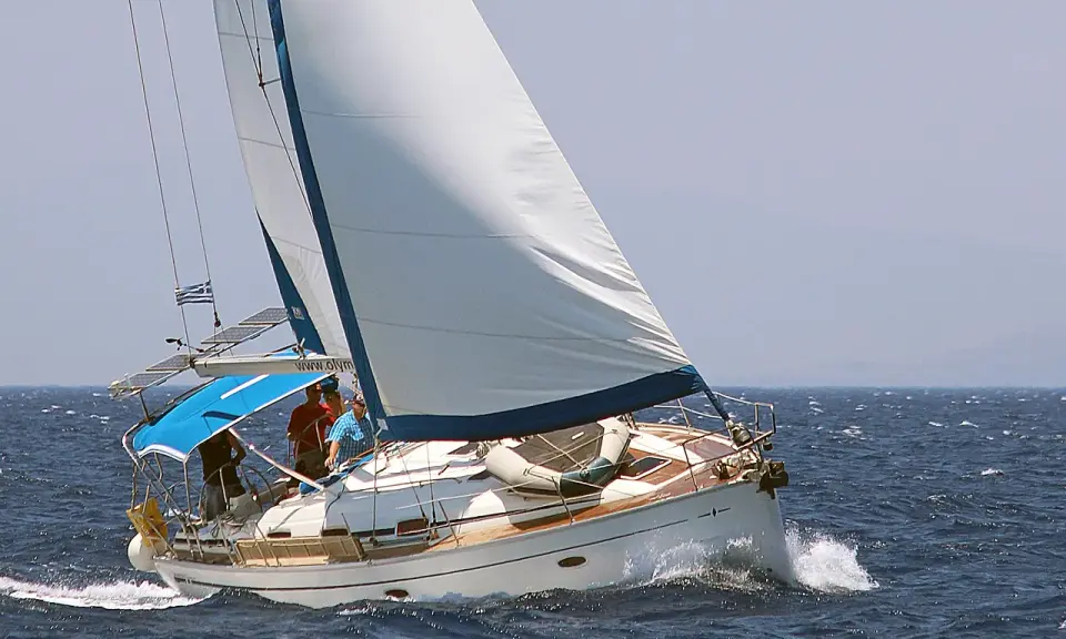 Un voilier blanc navigue sur une mer bleue agitée. L'équipage semble prendre un ris, ajustant les voiles pour mieux affronter le vent.