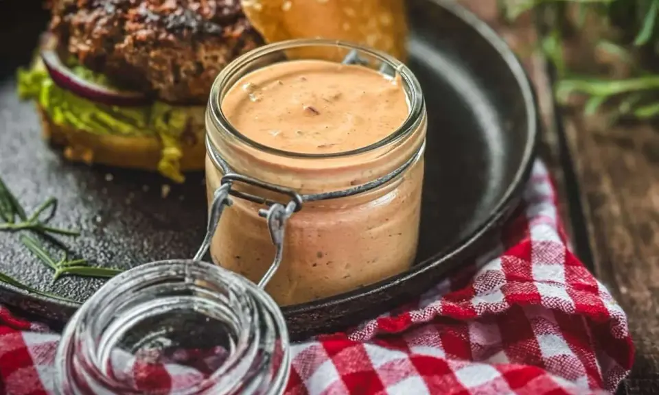 Leckere, cremige Sauce im Glas, perfekt zum schnelle Burger Sauce selber machen. Dazu ein saftiger Burger auf einem Gusseisen-Teller.
