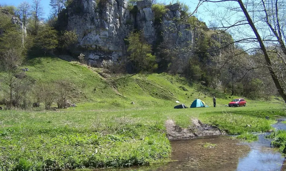 Malownicza dolina Kluczwody z rozbitymi namiotami, czerwonym samochodem i strumieniem.