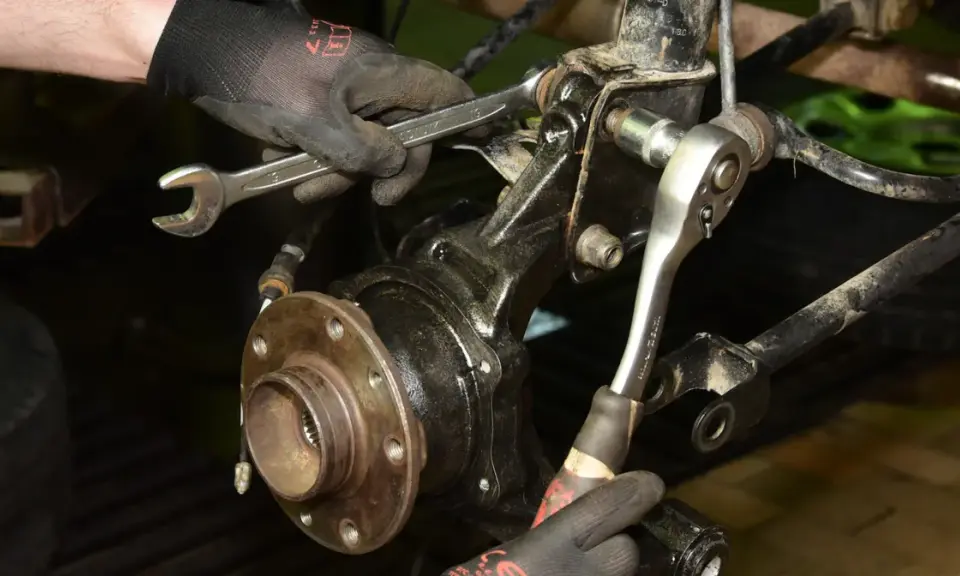 Mechanik w rękawiczkach używa kluczy do wymiany łożyska w piasty koła samochodu.