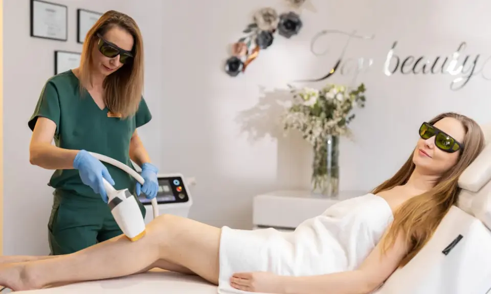Specjalistka wykonuje zabieg depilacji laserowej, sprawdzając przeciwwskazania fizykoterapii. Klientka leży na kozetce, obie w okularach ochronnych.
