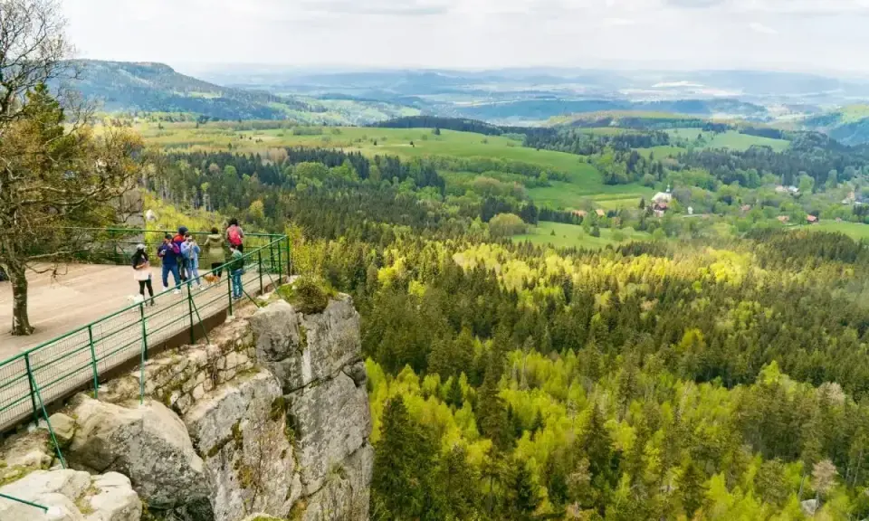 Grupa turystów podziwia rozległą panoramę Kotliny Kłodzkiej z platformy widokowej na skalistym zboczu.