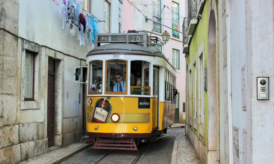 Gelbe straßenbahn lissabon fährt durch enge Gasse, Wäsche hängt über der Straße.