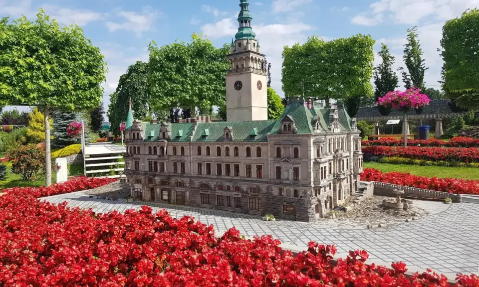 Miniatura ratusza z wieżą i zegarem, otoczona czerwonymi kwiatami. Jedna z wielu atrakcji Kotliny Kłodzkiej.