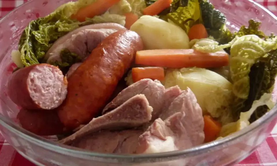 Un plat typique auvergnat : saucisses, porc, pommes de terre, carottes et chou savoyard mijotés dans un grand bol en verre.