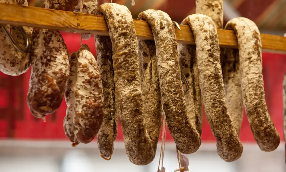Saucissons secs, une spécialité culinaire auvergnate, pendent sur un support en bois.