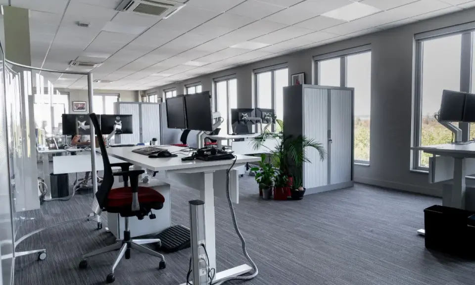 Aménagement moderne de bureaux en open space avec postes de travail équipés de plusieurs écrans, chaises ergonomiques et rangements.