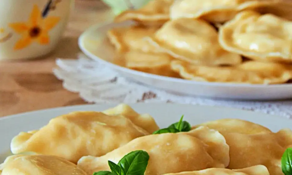 Słowackie pierogi z bryndzą na talerzu, ozdobione listkami bazylii.