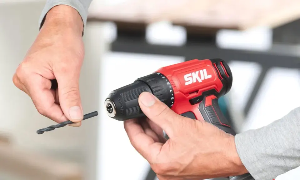 Man insertando una broca en un taladro inalámbrico rojo de la marca SKIL.