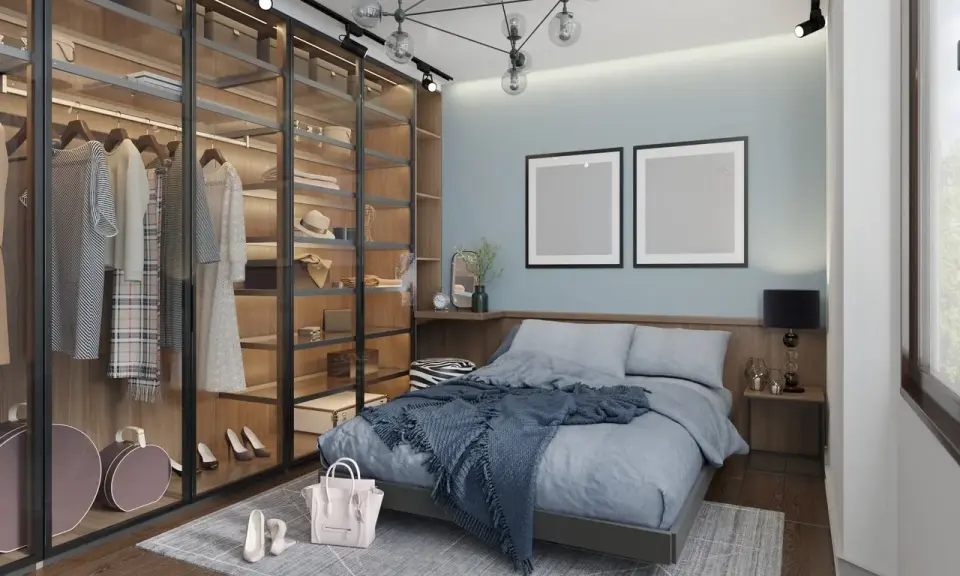 Chambre moderne avec dressing vitré bien organisé, lit bleu douillet et deux cadres vides au mur.
