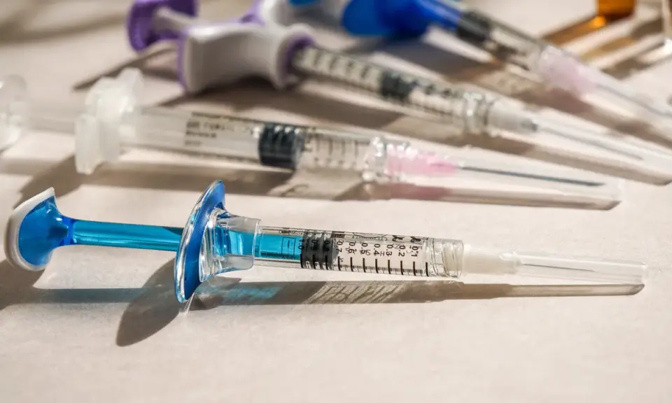 Flera sprutor med blå och lila detaljer ligger på en ljus yta. En spruta med blå kolv är i förgrunden, redo för vaccin i Colombia.