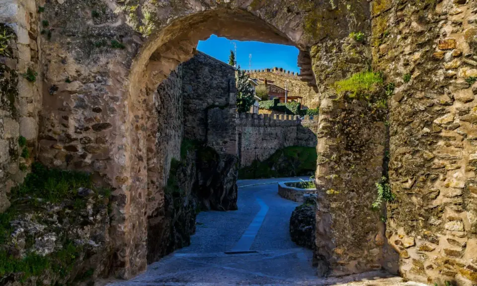 Un arco de piedra revela un camino empedrado y murallas, evocando la atmósfera de pueblos medievales cerca de Madrid.