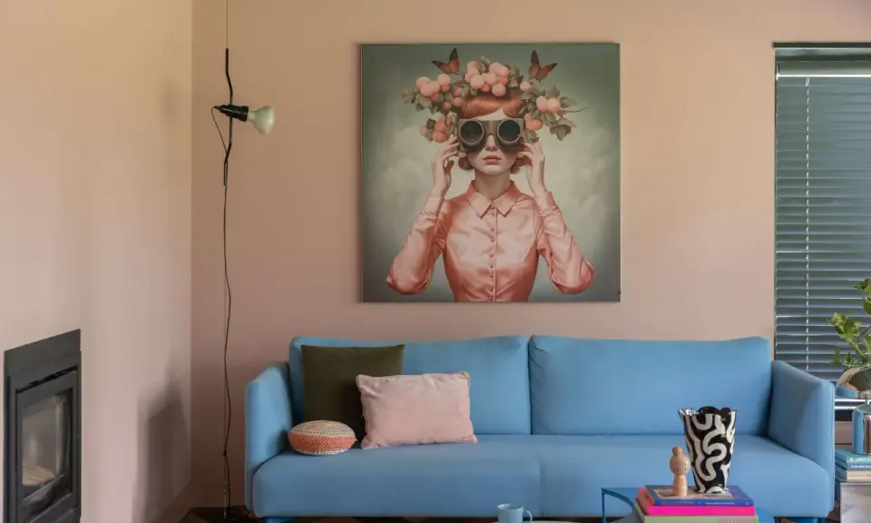 Ein hellblaues Sofa mit Kissen vor einem Bild, das eine Frau mit Blumenkranz und Schmetterlingen zeigt. Ein Beispiel für die Wohntrends 2026.
