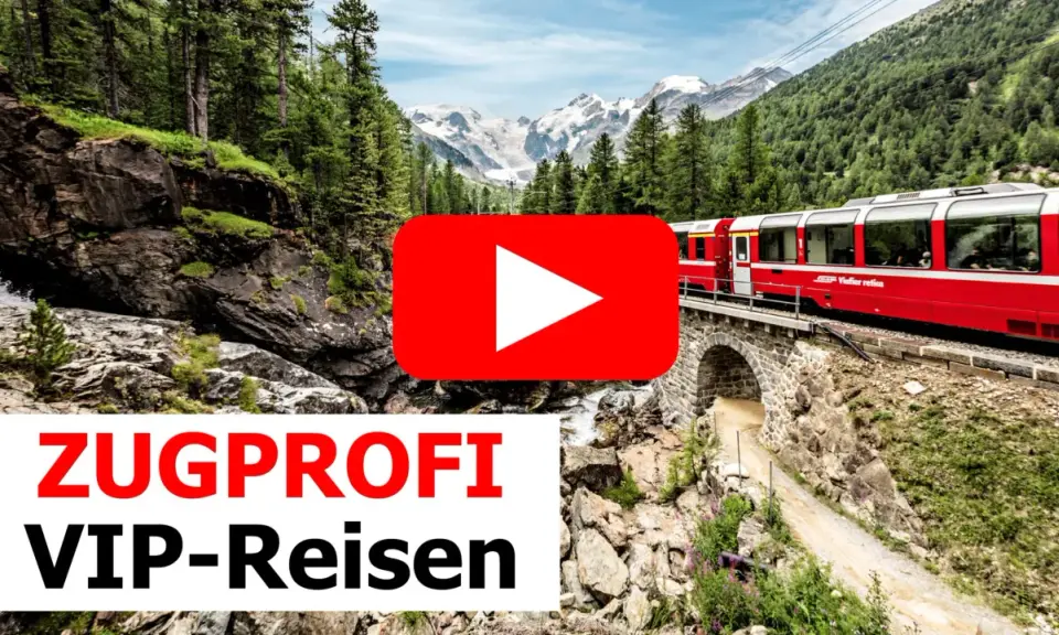 Ein roter Panoramazug fährt über eine Steinbrücke durch eine Berglandschaft mit Wäldern und schneebedeckten Gipfeln.