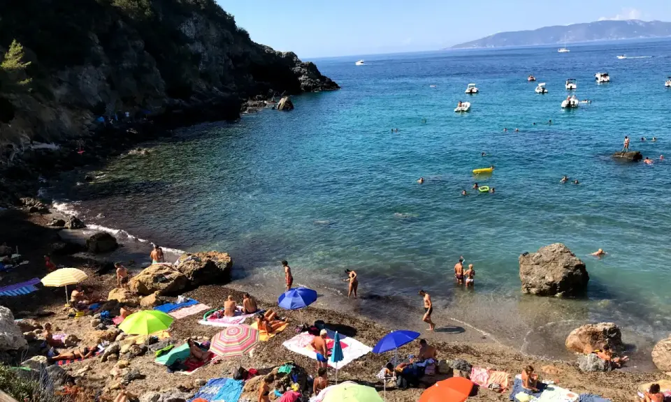 Spiaggia affollata con ombrelloni colorati e gente che nuota. Ecco come arrivare a Cala del Gesso per godersi questo mare cristallino.