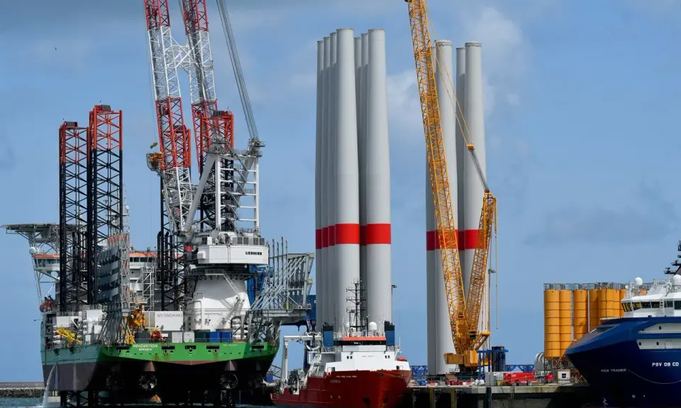 Un navire jack-up avec des grues massives se tient à côté de grandes tours d'éoliennes, prêt pour l'installation.