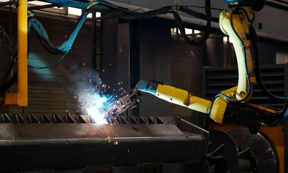 Braccio robotico giallo esegue saldatura, creando scintille luminose su un pezzo metallico grezzo.
