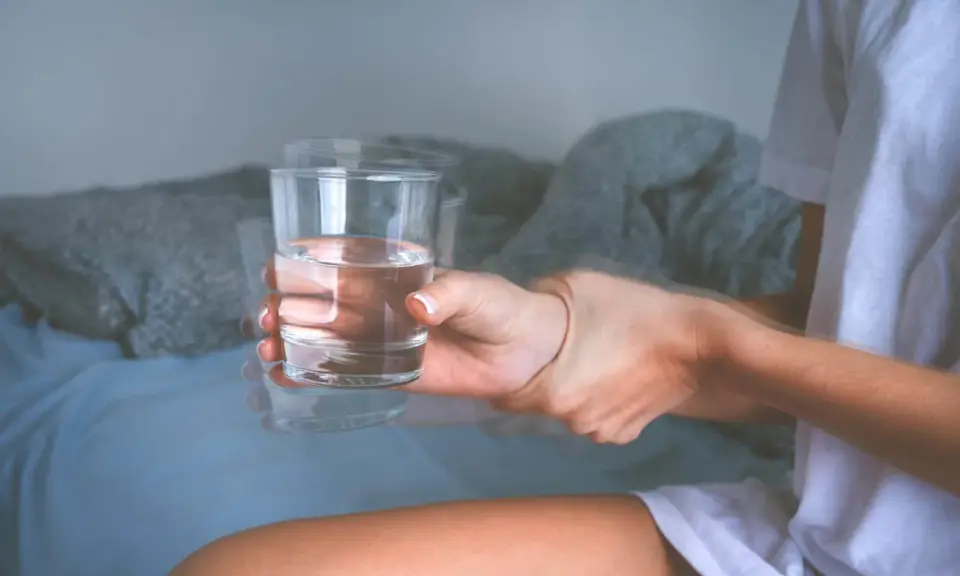 Drżąca ręka trzyma szklankę wody. Objawy mogą wskazywać na atak padaczki alkoholowej. Co robić?