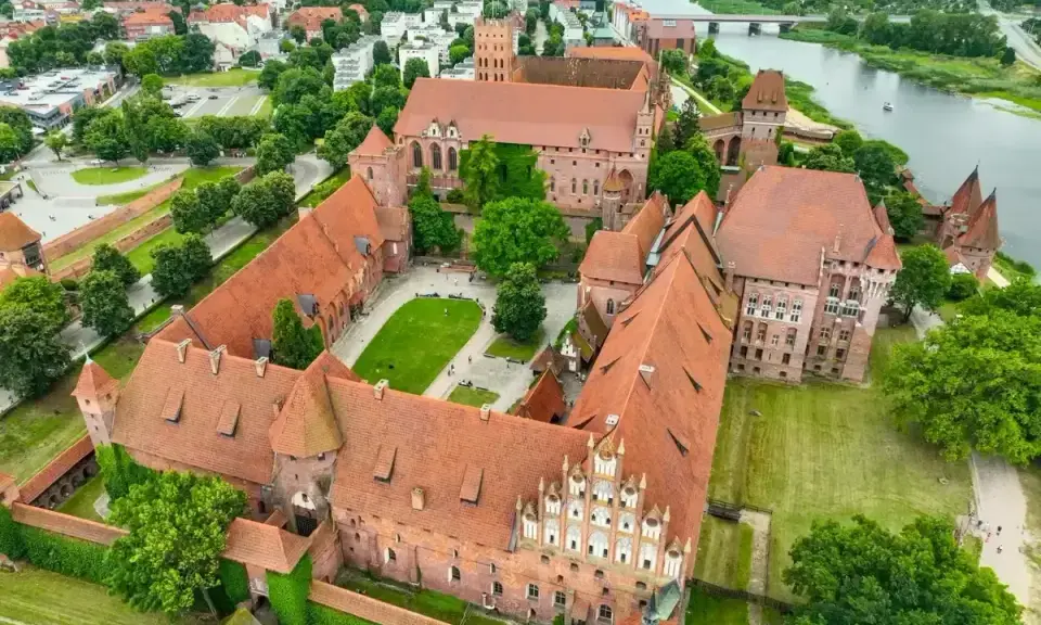 Malbork, największy zamek w Polsce, rozciąga się wzdłuż rzeki Nogat. Jego ceglane mury i liczne wieże tworzą imponujący krajobraz.