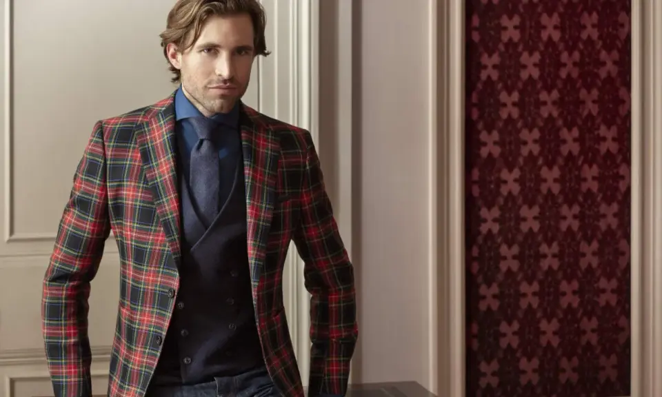 Man in a festive tartan blazer, dark blue shirt, tie, and vest. This is what holiday attire looks like.