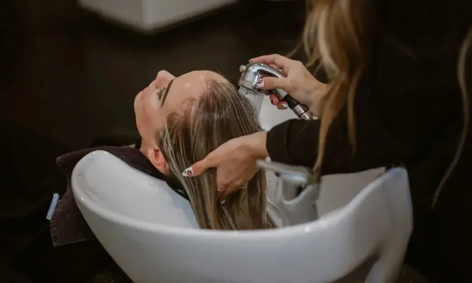 Una parrucchiera sciacqua i capelli di una cliente in un lavatesta, mostrando come lavare i capelli senza shampoo.