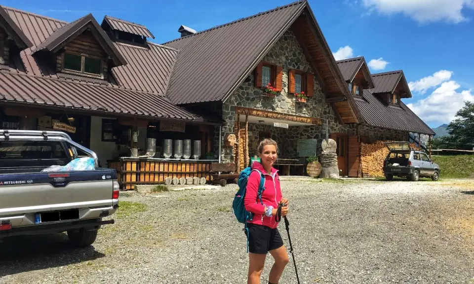 Ragazza con zaino e bastoncini da trekking davanti alla malga Lavareit, con un pick-up e un'auto parcheggiati.