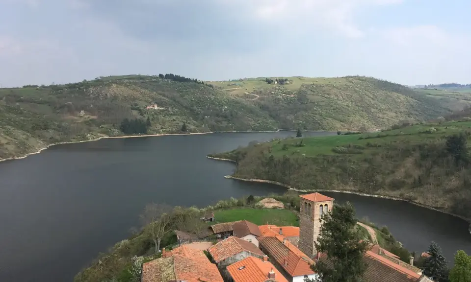 Villaggio pittoresco con tetti rossi e campanile affacciato su un lago serpeggiante, incastonato tra colline verdi vicino a Roanne, Francia.