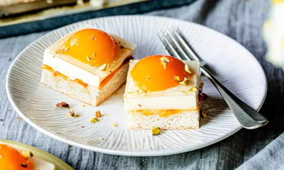 Zwei exquisite Stücke spiegeleikuchen mit pudding, garniert mit Pfirsich und Pistazien, auf einem Teller mit einer Gabel.