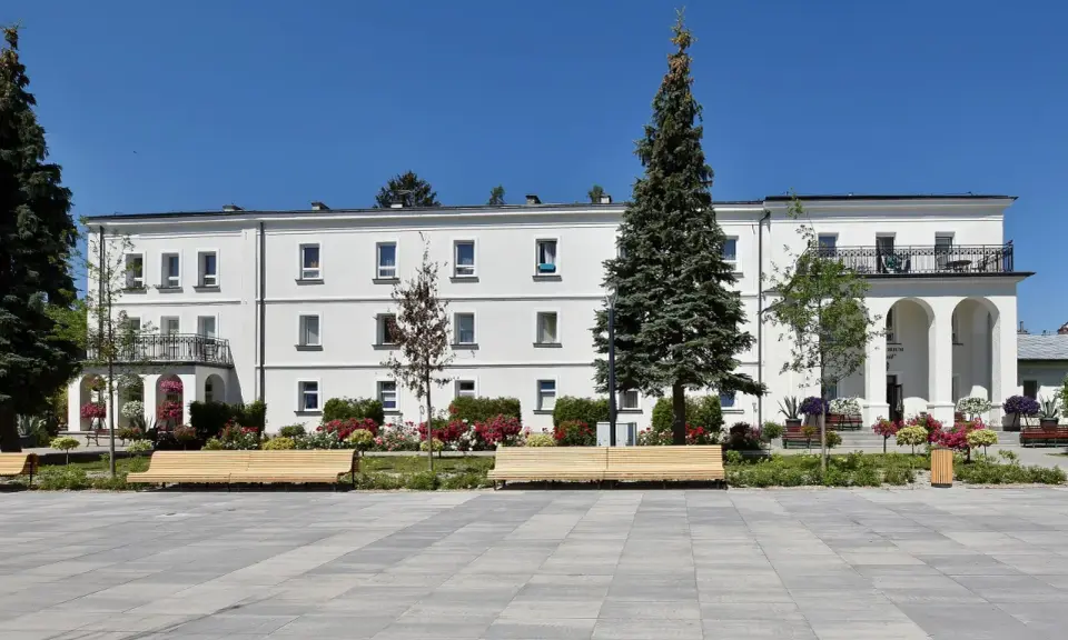 Sanatorium Świt w Solcu-Zdroju, biały budynek z balkonami i łukami, otoczony zielenią i kwiatami.