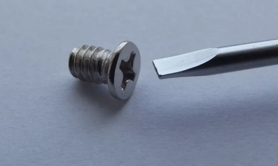Tornillo metálico con cabeza de estrella y destornillador plano listo para ayudar a como quitar un tornillo pasado.