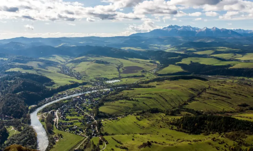 Widok na dolinę z rzeką i miasteczkiem, w oddali majaczą góry Tatry, które przypominają trzy korony. Wysokość widoku zapiera dech.