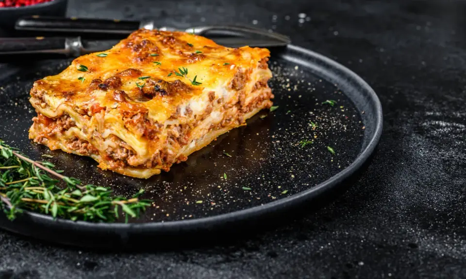En bit gyllene lasagne på en svart tallrik, perfekt comfort food med köttfärs och ost.