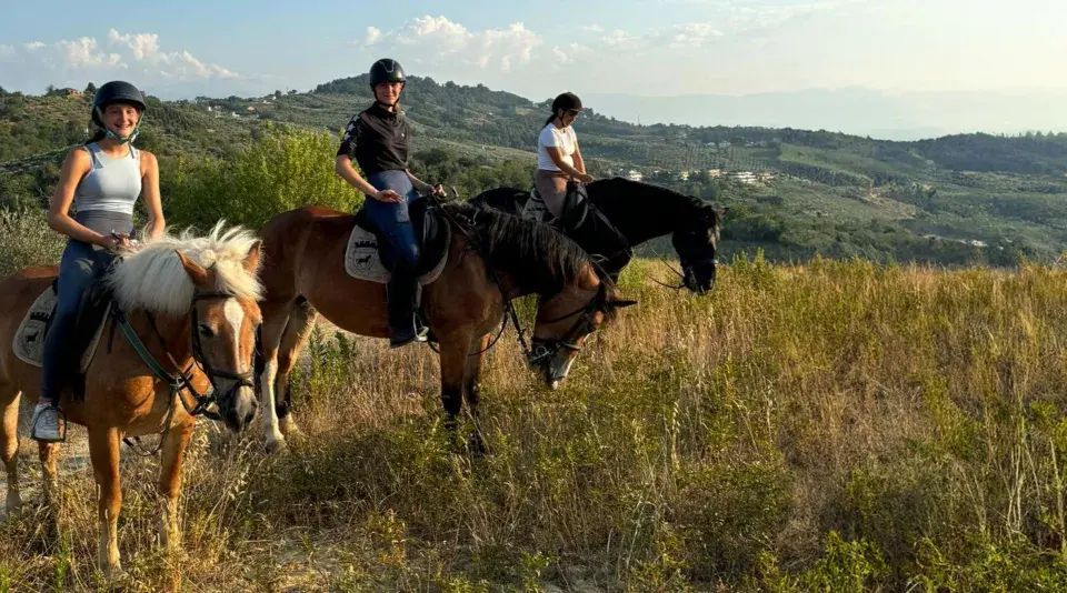 Tre ragazze in sella a cavalli godono di splendide passeggiate a cavallo in Abruzzo, tra colline verdi e cielo azzurro.